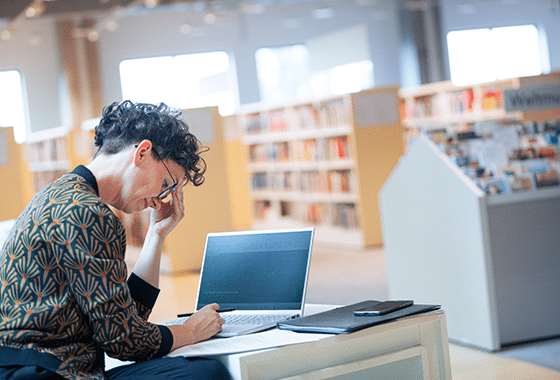 Verena Smit arbeitet vor dem Hintergrund einiger Bücherregale konzentriert an ihrem Laptop.