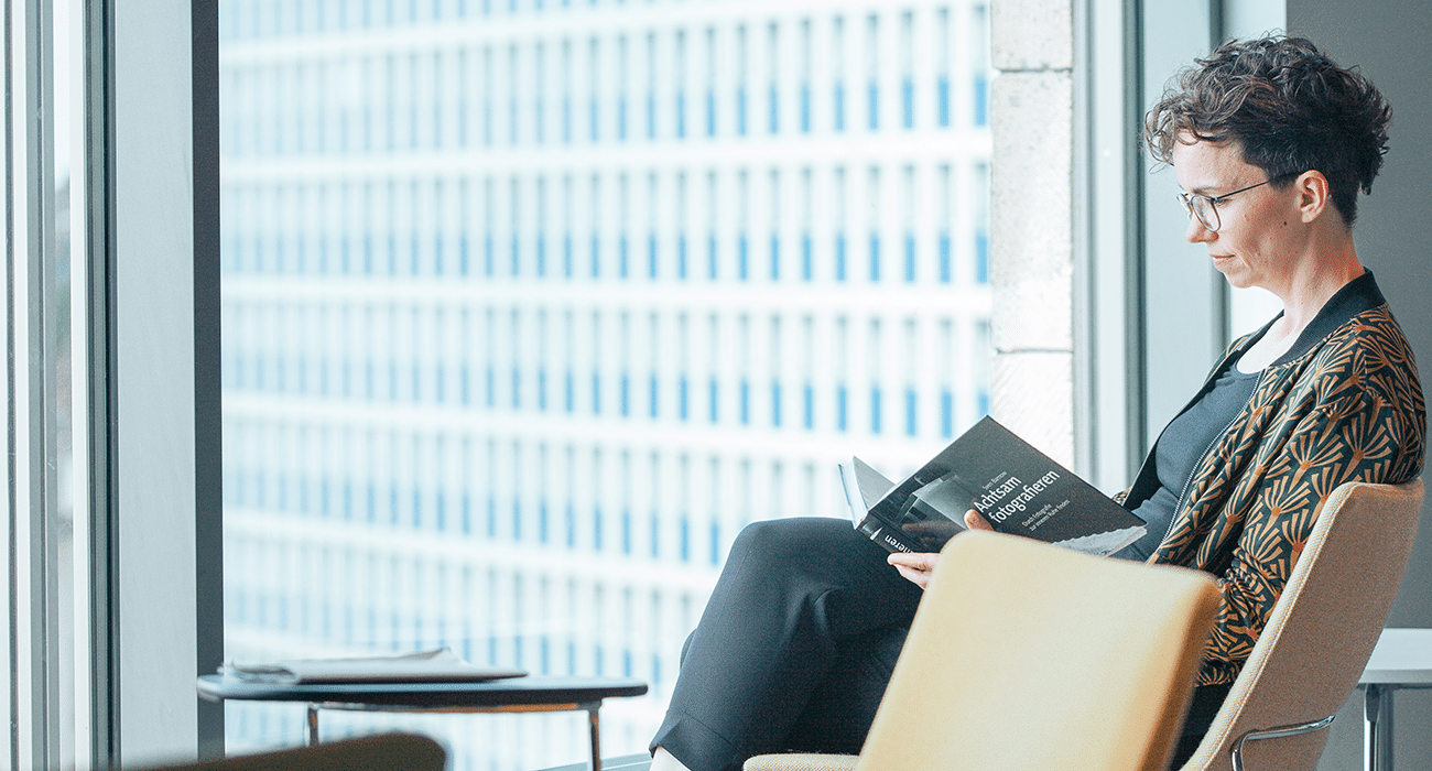 Verena Smit sitzt vor einem großen Fenster in einem Sessel und liest in einem Buch.