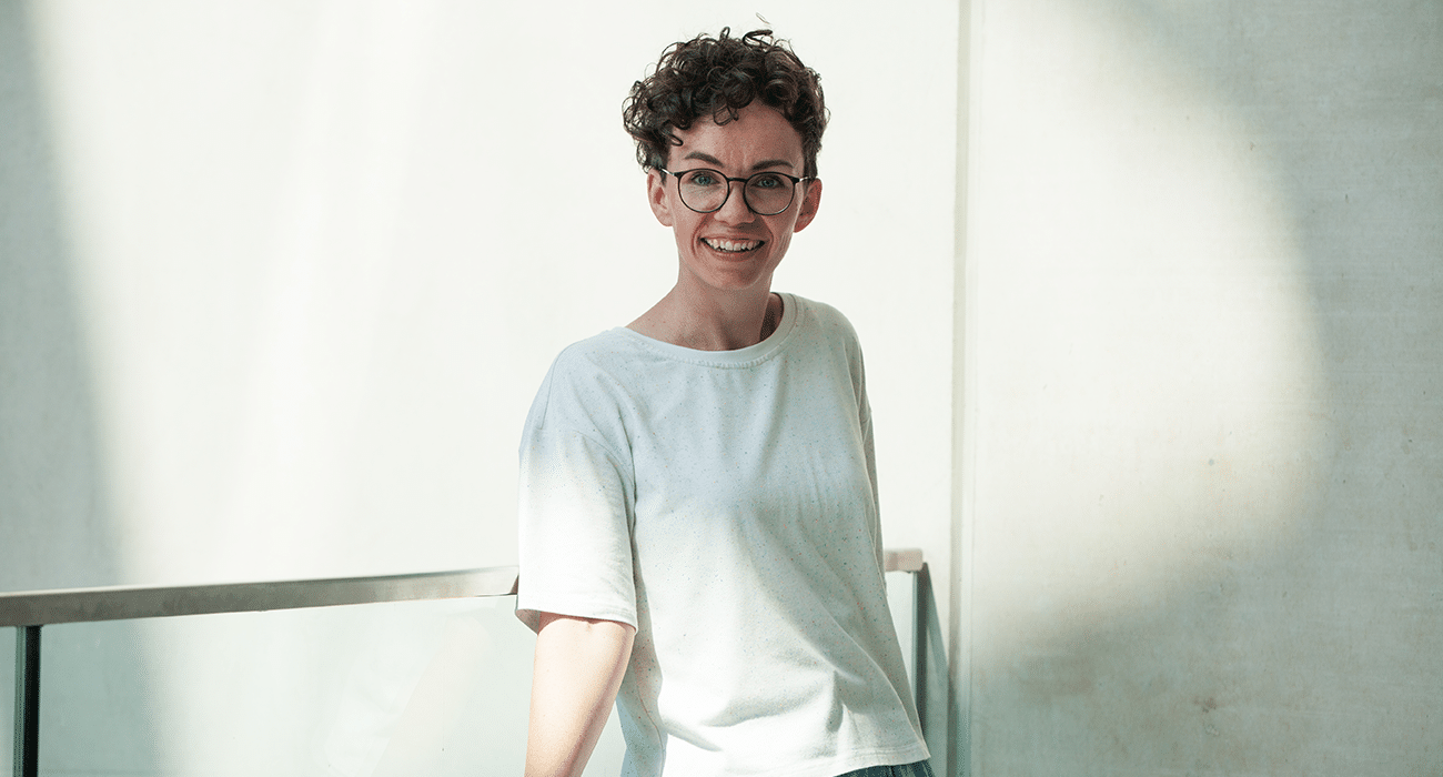 Verena Smit lehnt sich an ein Treppengeländer und lächelt direkt in die Kamera.