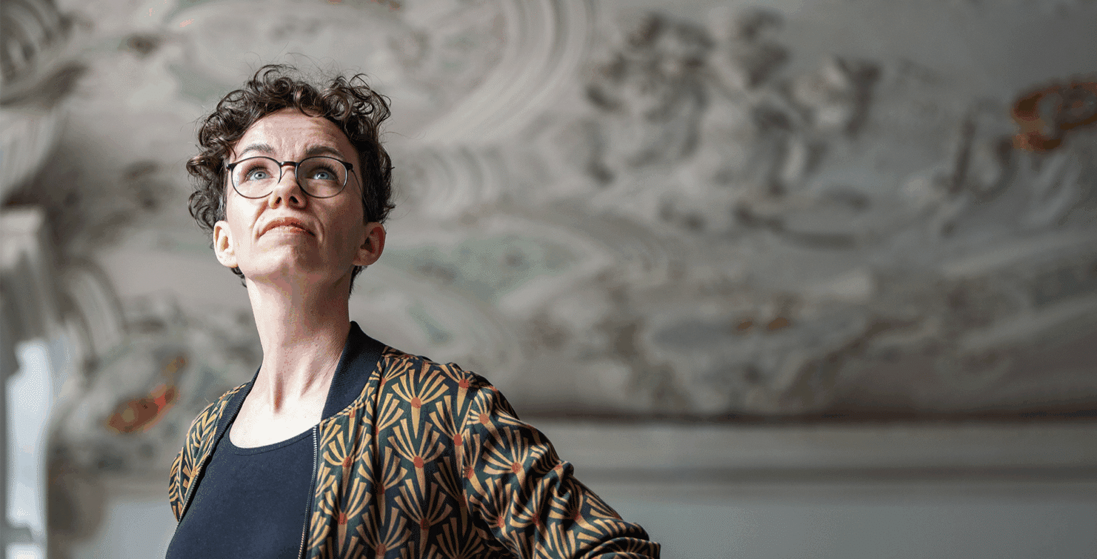 Verena Smit betrachtet die Stuckdecke eines historischen Gebäudes.