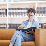 Verena Smit sitzt auf dem Sofa einer Bibliothek vor einem Bücherregal mit kunsthistorischer Literatur und betreibt Recherchen.