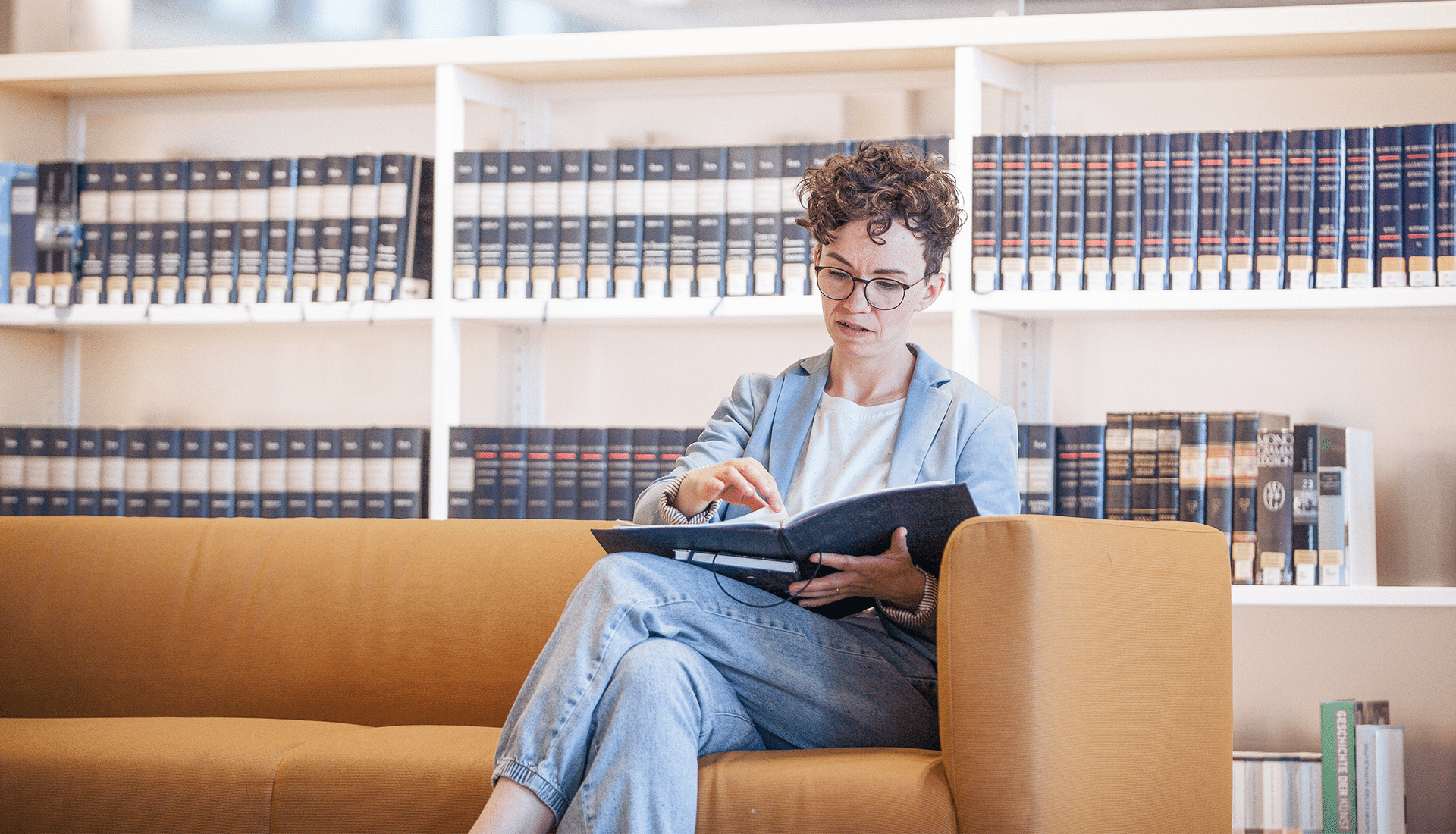 Verena Smit sitzt auf dem Sofa einer Bibliothek vor einem Bücherregal mit kunsthistorischer Literatur und betreibt Recherchen.